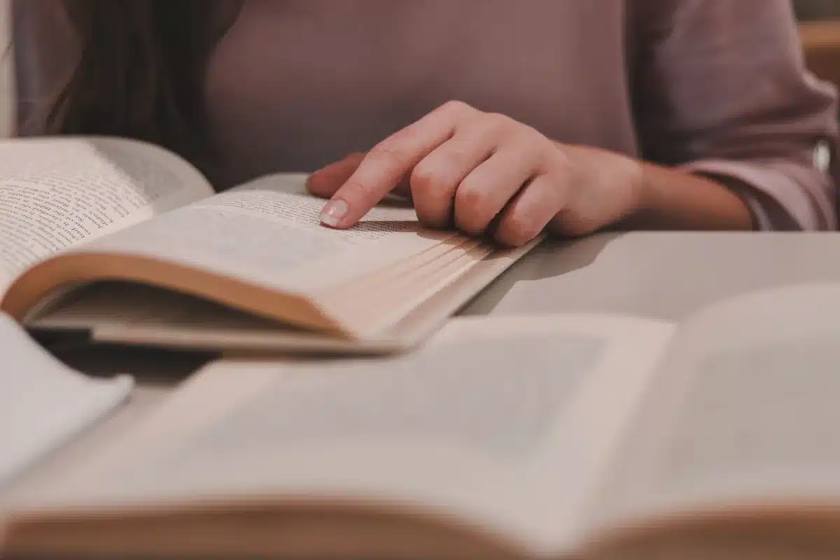 A woman reading through manuscript pages and documents at a desk in a study.