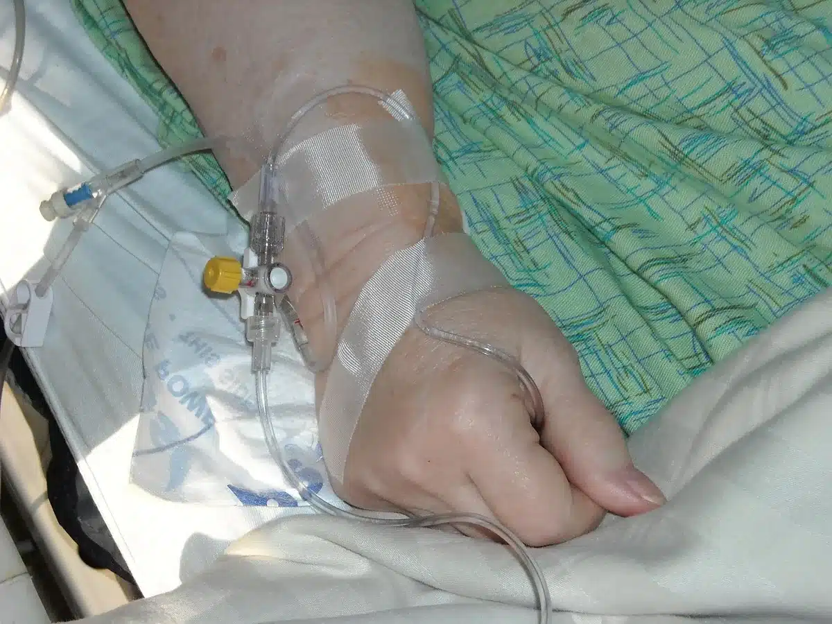 Silhouetted hands on a hospital bed with morning light from a window and blurred medical equipment in the background