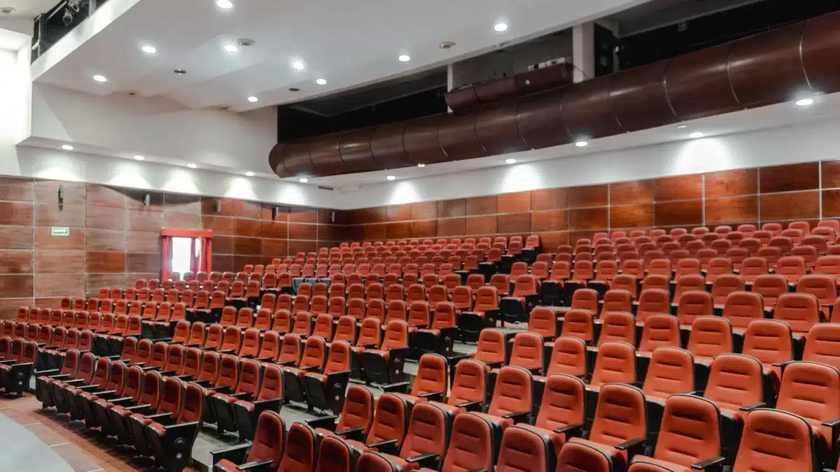 Empty high school auditorium stage with silhouetted figures and warm stage lighting