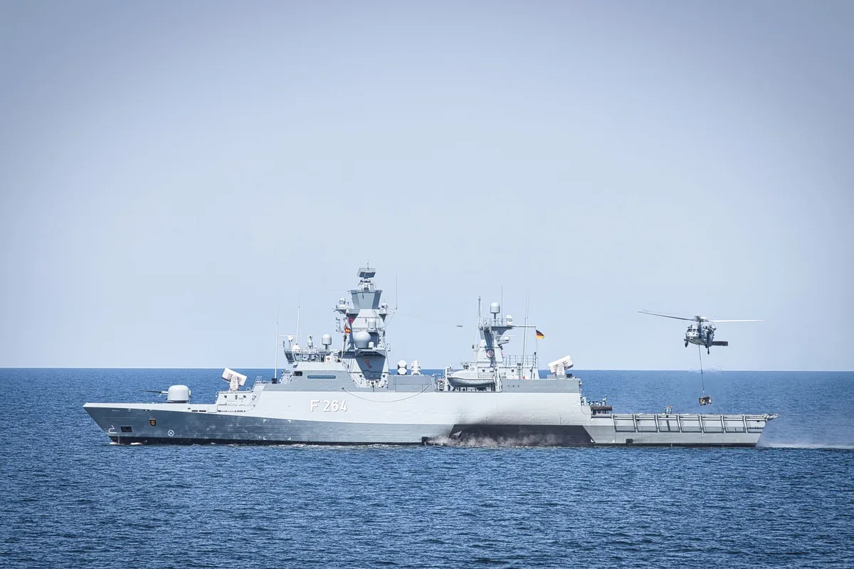 A crowded rescue boat speeding across rough waters with a military helicopter pursuing overhead