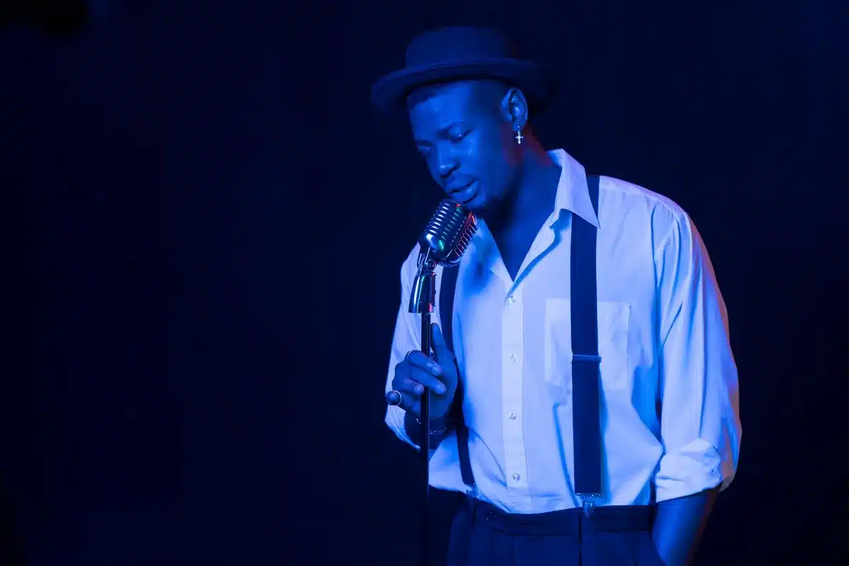 Warm stage lighting illuminates an empty microphone stand on a vintage variety theatre stage