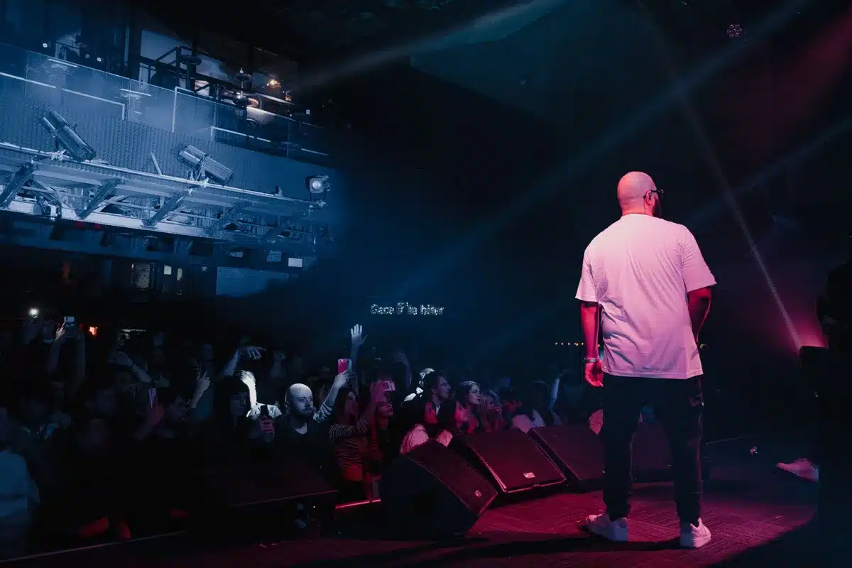 Dimly lit nightclub stage with microphone and anonymous crowd silhouettes