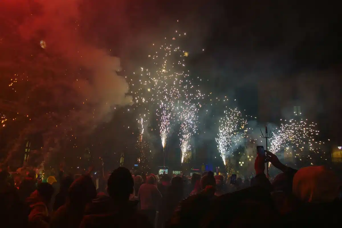 Crowd of people celebrating together in a city plaza at night with raised hands and city lights
