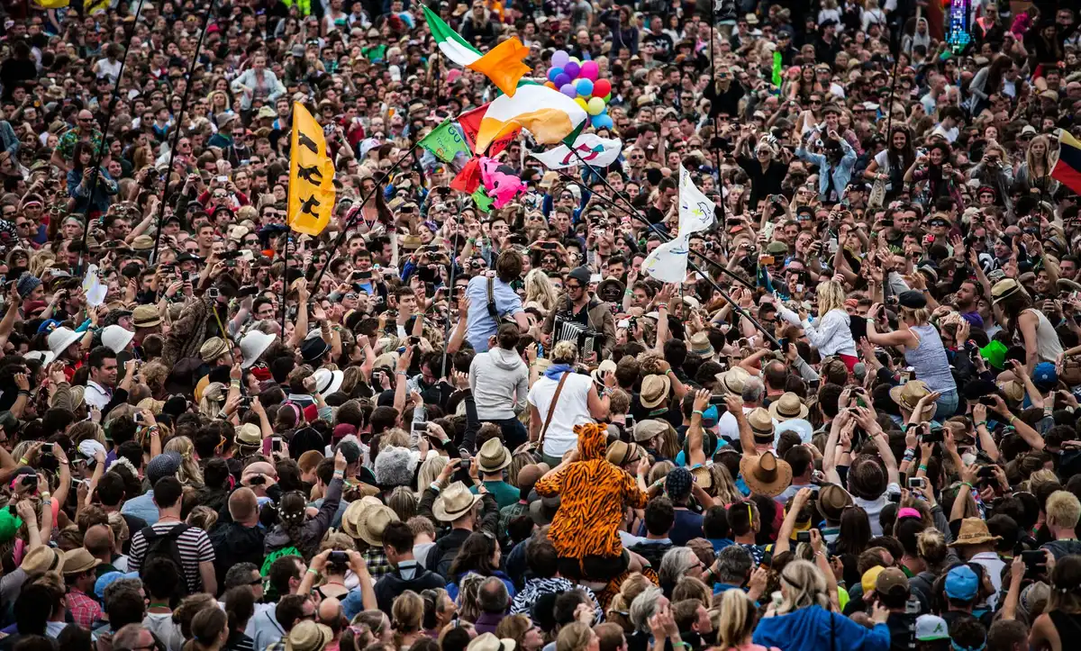 Crowd of festival-goers dancing under stage lights at an outdoor summer music event in a park