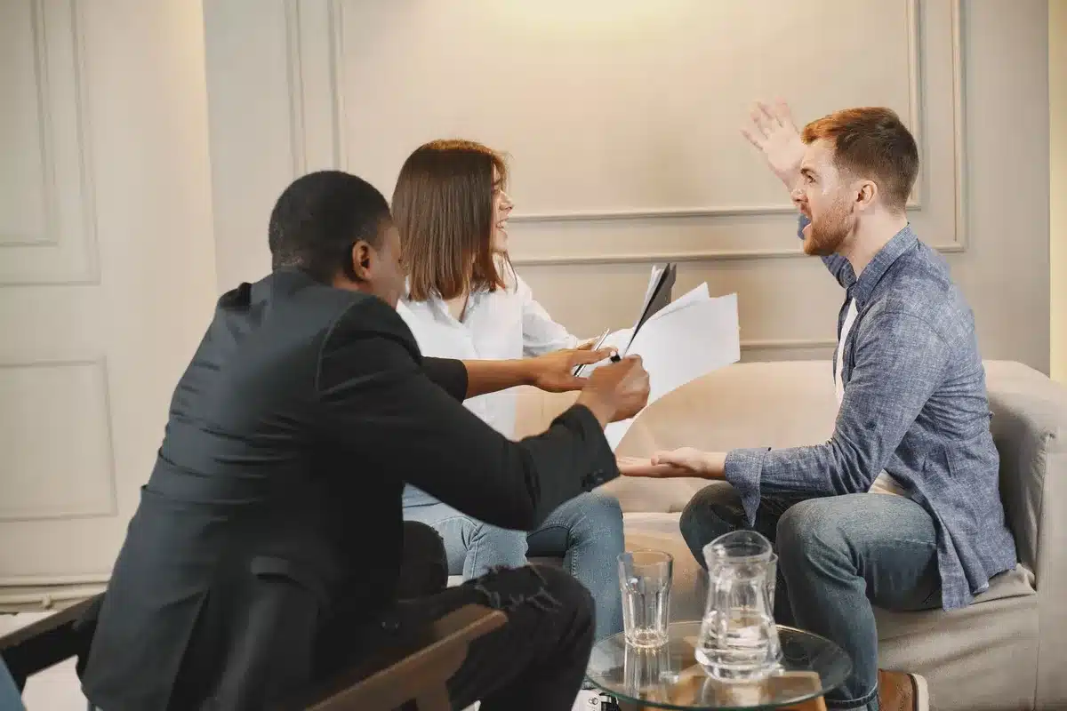 Two people at a conference table in disagreement, one standing and one seated, showing tension and conflict in a corpora