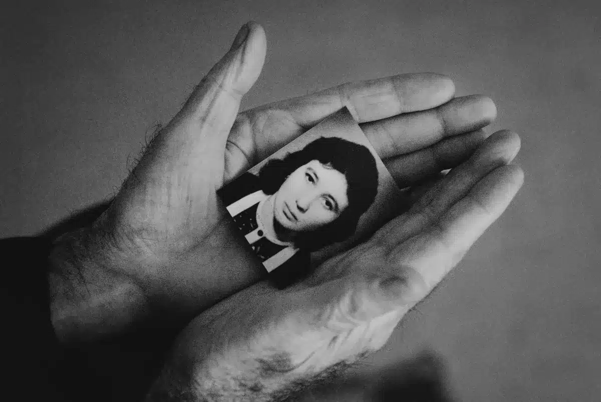 Elderly woman's hands resting on a table with family photos and personal mementos in soft light