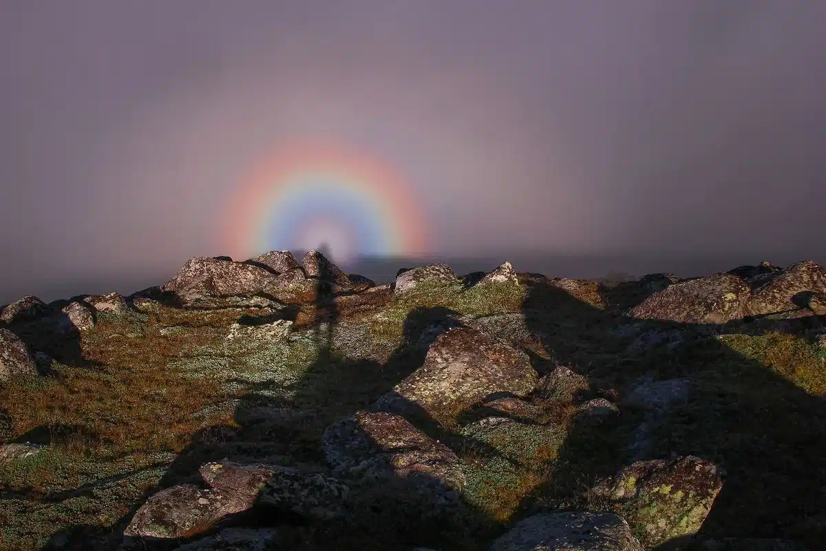 Silhouette of a person standing beneath a vibrant rainbow in a dreamy natural landscape
