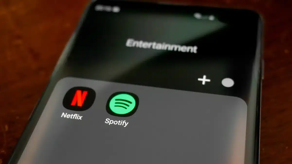 a small table lamp beside a smartphone showing a generic music app interface, screen glow on a wooden bedside table, no logos or text