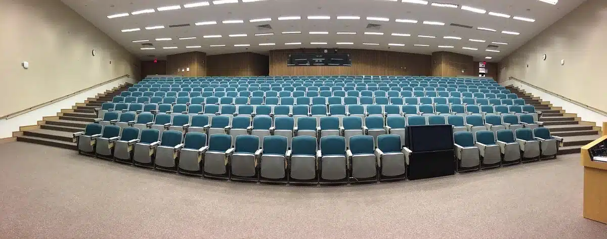 An empty elementary school auditorium with rows of small chairs, a single unbranded music stand and a set of orchestral chairs on stage hinting at an impending performance