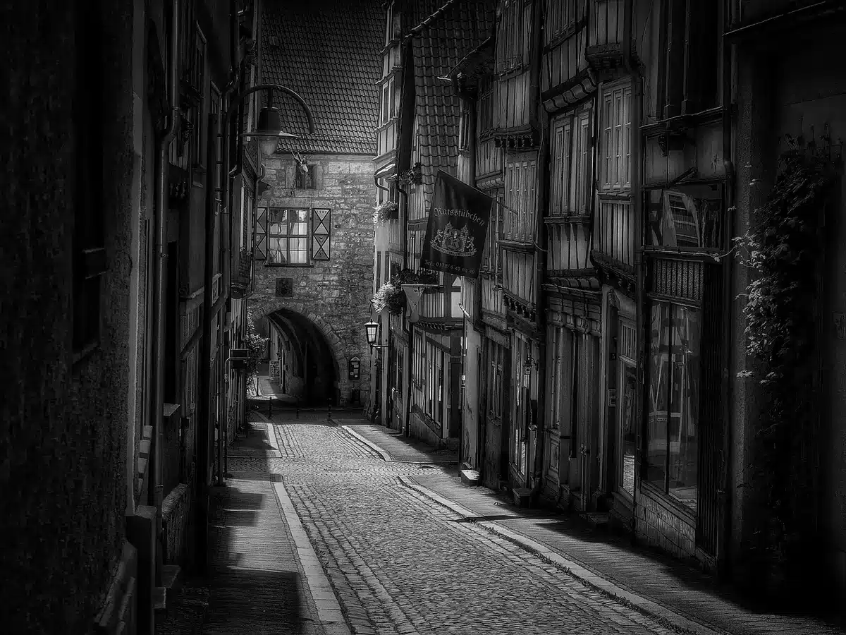 A dimly lit vintage alley with a single abandoned umbrella and a discarded fedora under a streetlamp, wet cobbles reflecting neon; anonymous shadow suggests a lurking figure