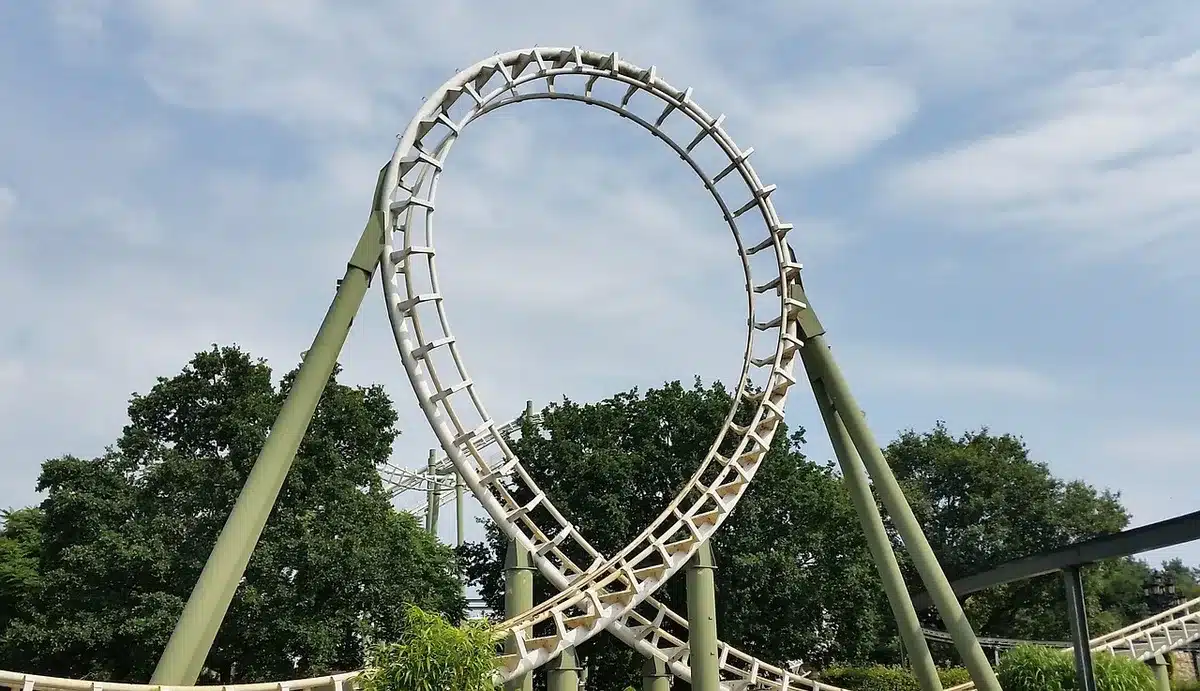 A deserted amusement-park walkway with a distant roller-coaster silhouette against a late-afternoon sky