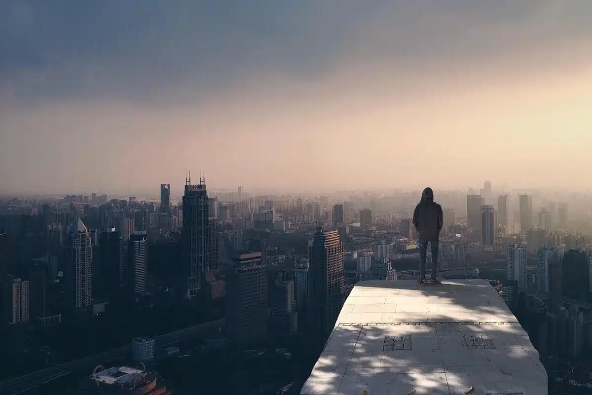 Silhouetted figure in dark catsuit crouched on rooftop at dusk with city lights below