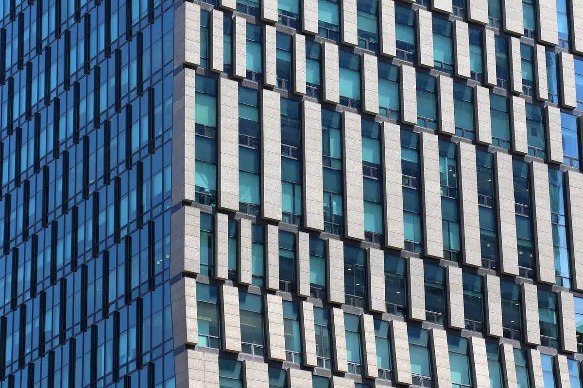 A modern corporate office lobby with floor-to-ceiling windows overlooking a cityscape, glass conference tables reflecting soft light, and an empty corridor suggesting the scale and contemporary nature of a newly merged enterprise headquarters.