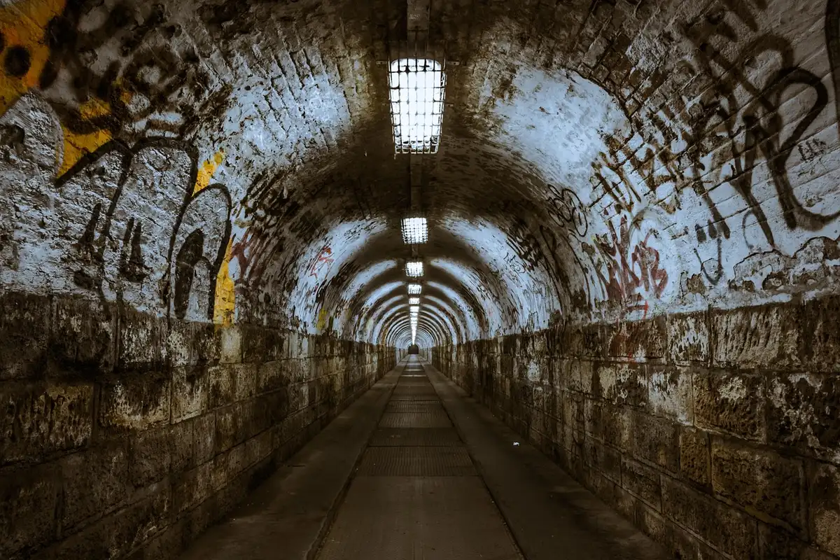 A dimly lit convention corridor with empty vendor tables and a lone poster stand bearing a generic comic-salon graphic, hinting at an imminent reveal