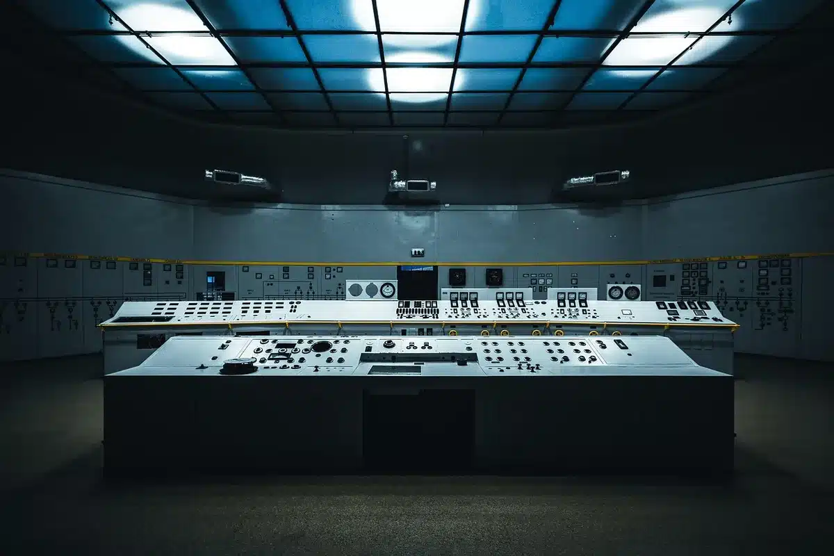 A close-up of an empty panel room with stacked chairs and a blank projector screen, a single microphone on the table, suggesting a forthcoming panel announcement