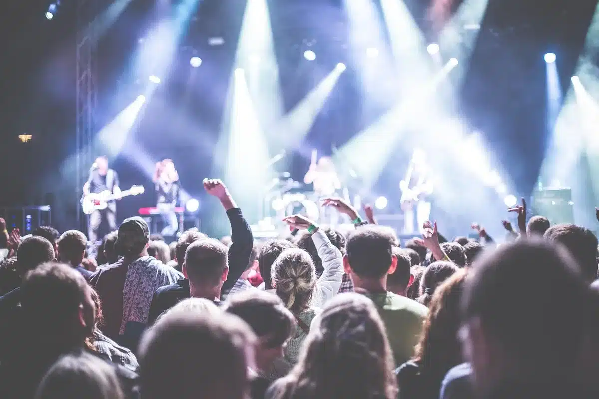 Anonymous crowd in a theater applauding under warm house lights, blurred faces and raised hands