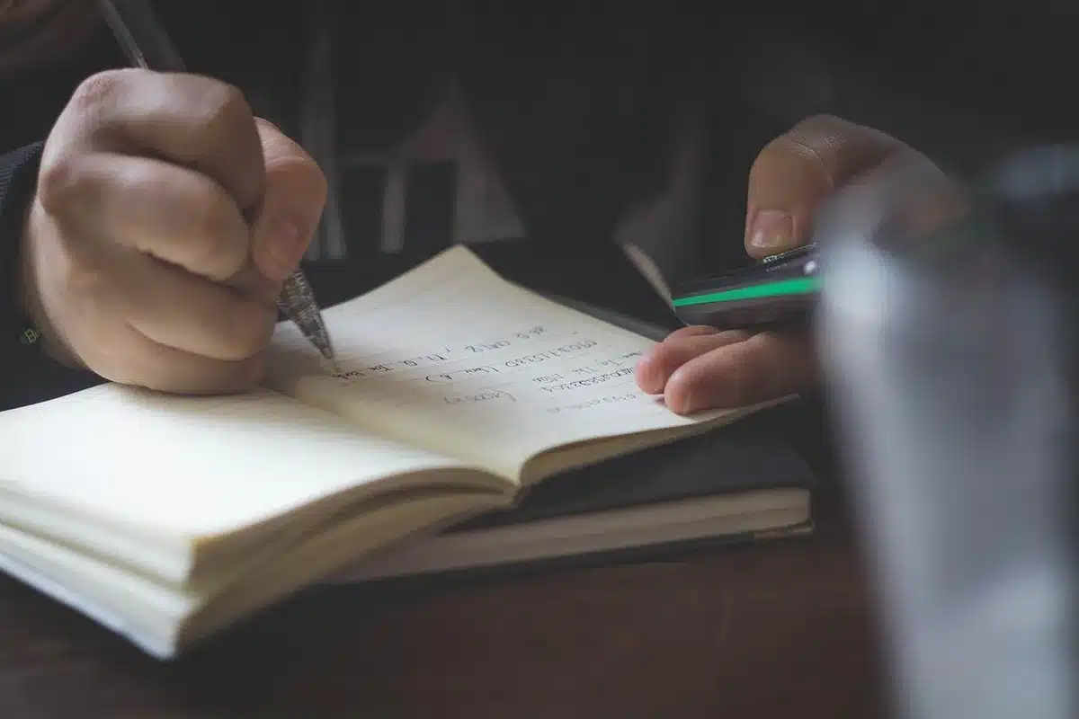 Anonymous students in a dim classroom adjusting a camera and taking notes