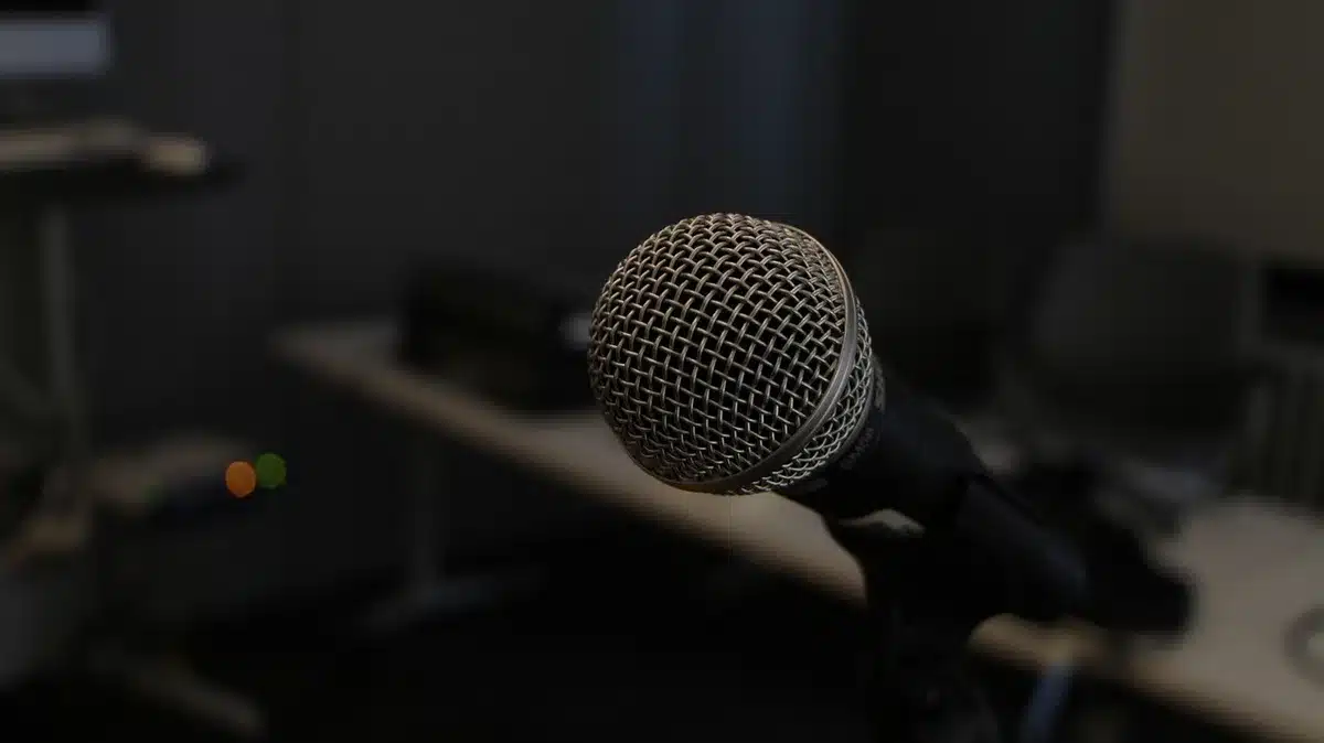 Backstage close-up of stacked unbranded speakers and coiled cables beside an empty stage door, ambient stage lights in the background, no people or logos