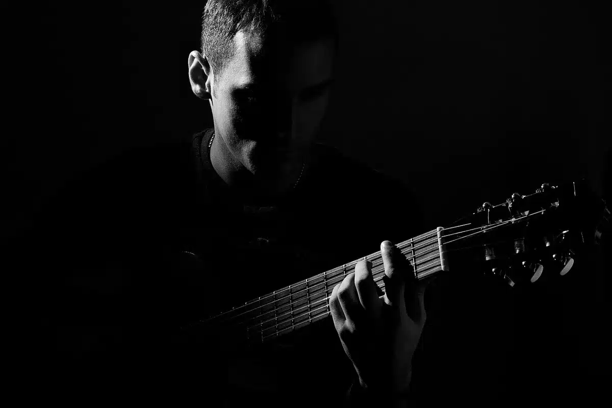 Silhouette of guitar and mixing console in a dim studio, hands on knobs
