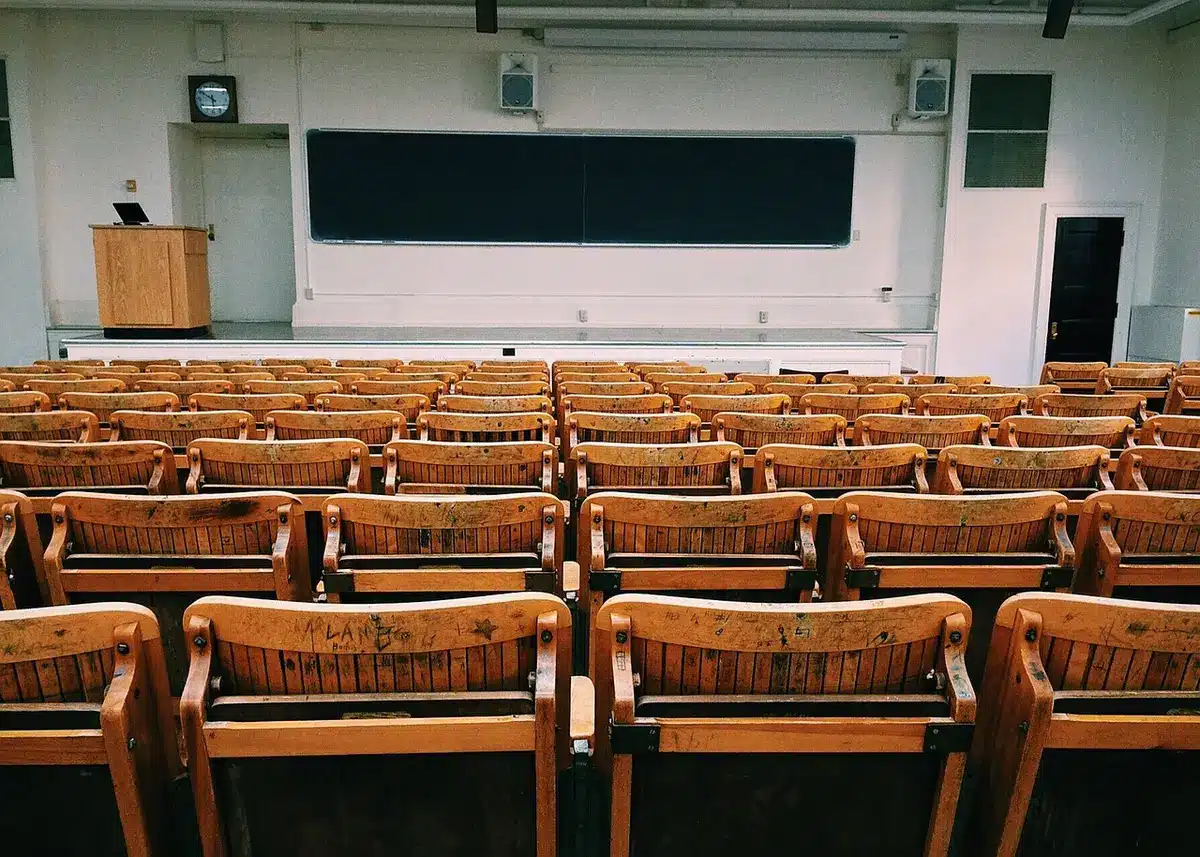 Empty classroom with chairs arranged in a circle, a single notebook and pen on a desk, soft natural light, symbolizing youth education and safe learning spaces