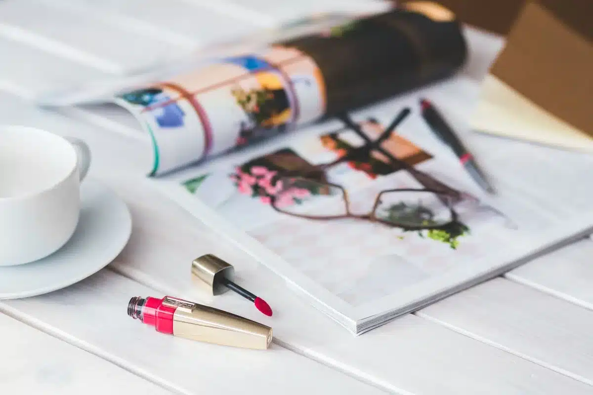 Hands sorting print magazines on an editorial desk with coffee and bookshelf