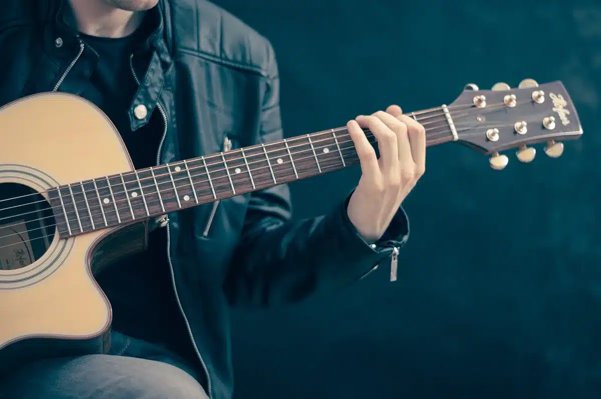 An empty small-stage performance area with a single microphone stand and an unbranded acoustic guitar leaning against an amp, warm stage lights dimmed but focused on the instrument, suggesting resilience and renewed hope