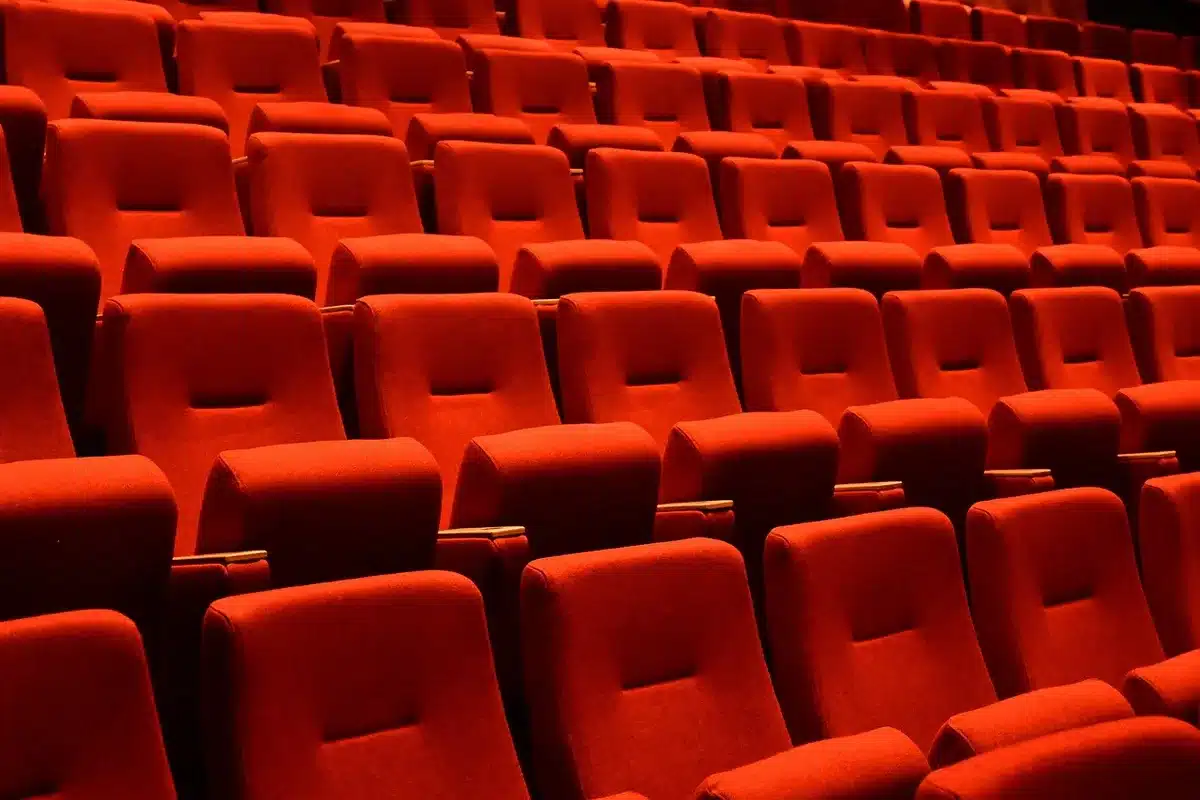 Empty cinema seats illuminated by golden stage lights in an auditorium.