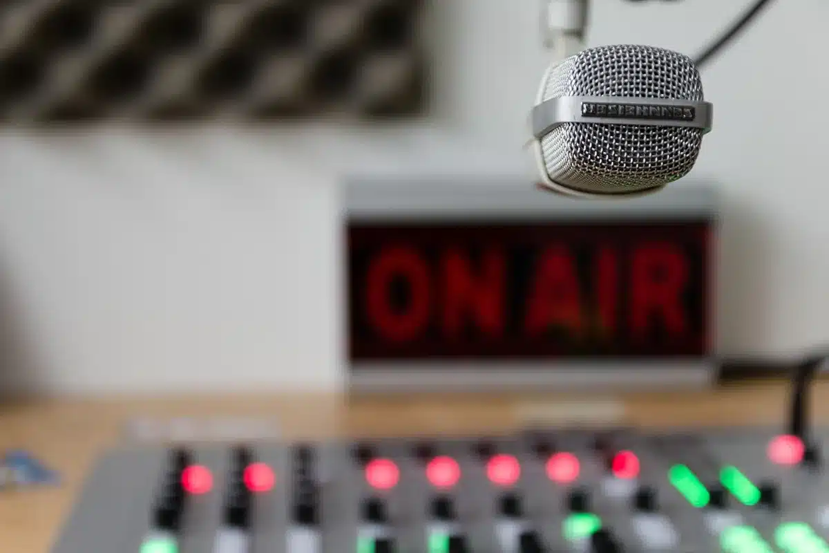 Silhouette of a hand holding a microphone in a dim recording studio with soft colored lighting.