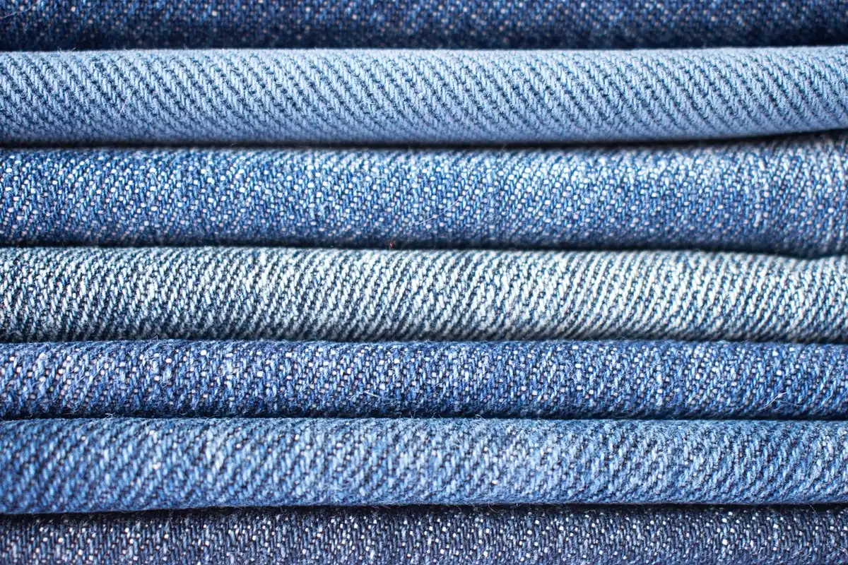 Folded Calvin Klein denim jeans in various washes stacked on a clean white surface, showing texture and fabric detail, minimalist product styling