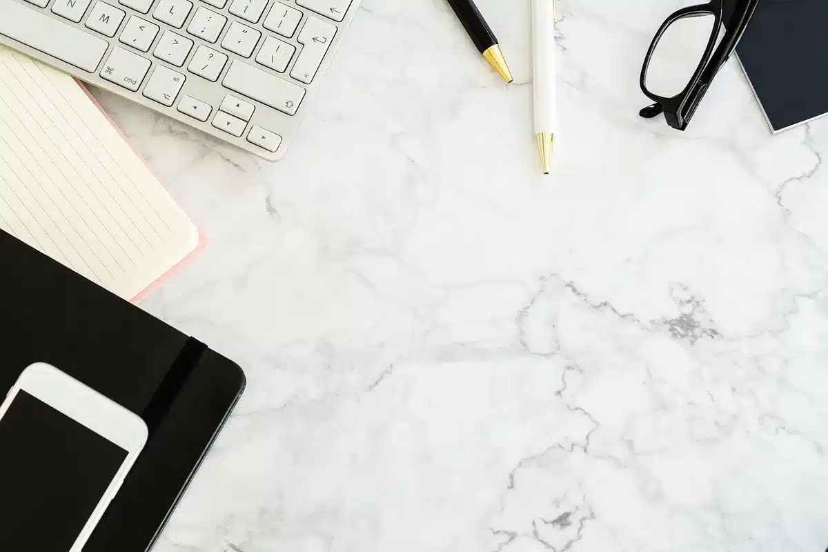 Close-up of an unbranded distributor office desk with press releases and a blank DVD case, a computer monitor showing distribution spreadsheets blurred in the background