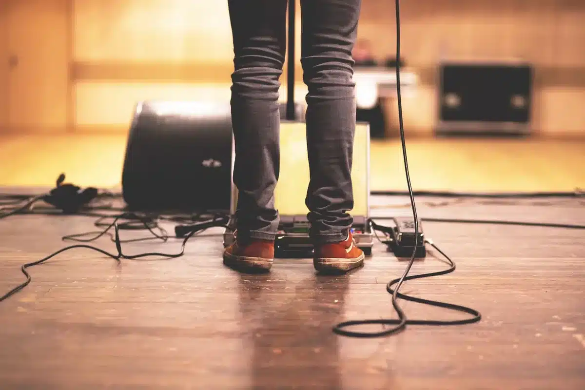 An empty stage edge with a lone microphone stand and a single pair of discarded unbranded flats beside it, soft stage lighting and a hint of crowd beyond — intimacy, clarity