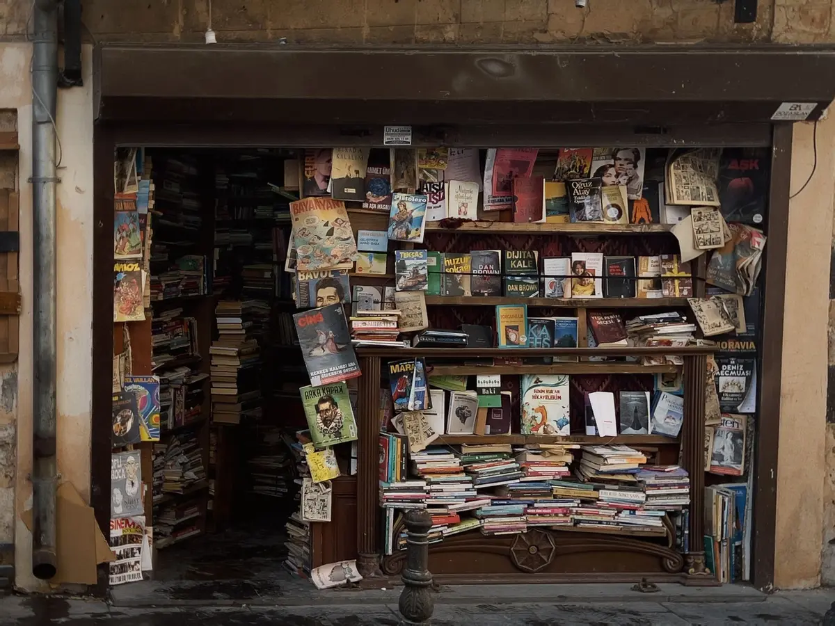 anonymous reader sitting at a café table, a stack of unbranded graphic novels and a steaming cup on wood surface