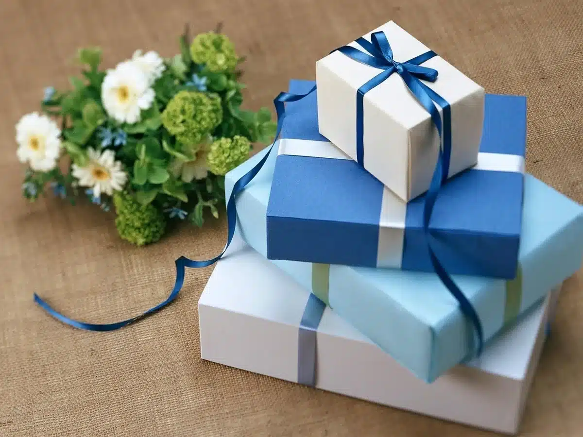 An anonymous close-up table spread of unbranded gift items—a small instant camera, a compact 3D-printing pen, a stack of colorful craft beads and a generic wearable blanket—arranged for holiday gift-wrapping; no text or logos