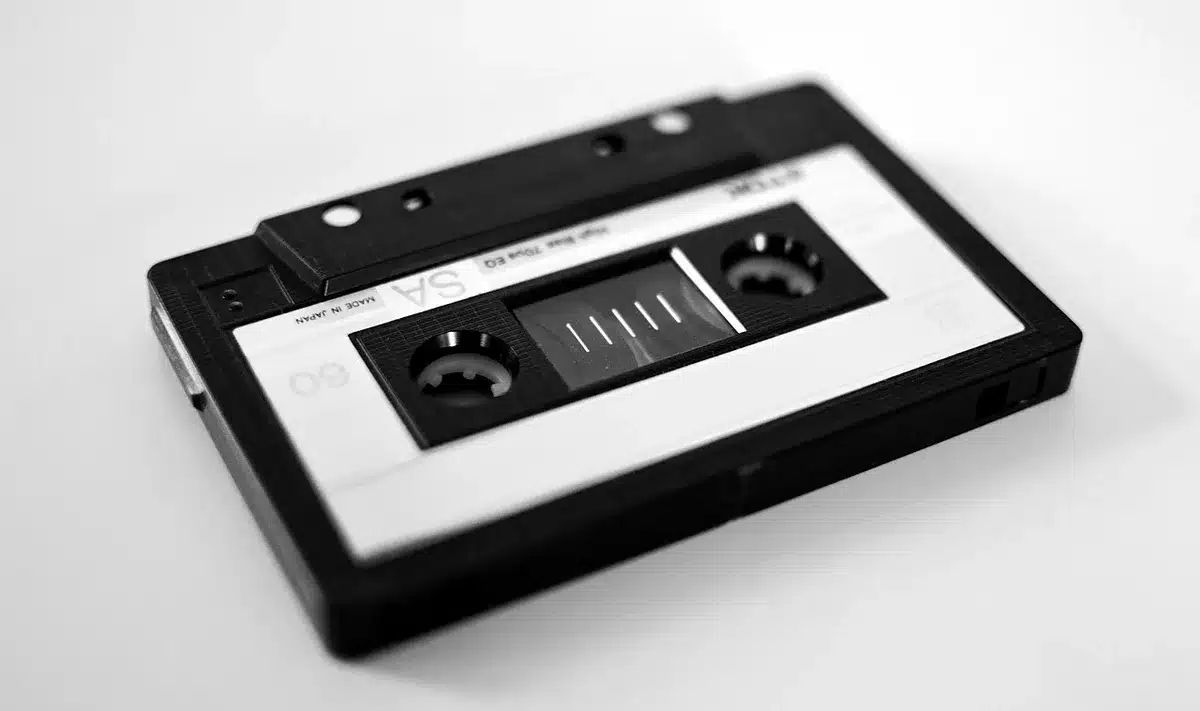 A compact cassette and a CD jewel case overlapped on a wood table, a generic printed lyric sheet partially visible but unreadable — a tactile snapshot of 90s listening formats