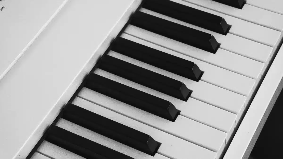 A single unbranded upright piano keyboard in a practice room, a sheet of music showing three sharp symbols visible on the staff, soft natural light from a side window