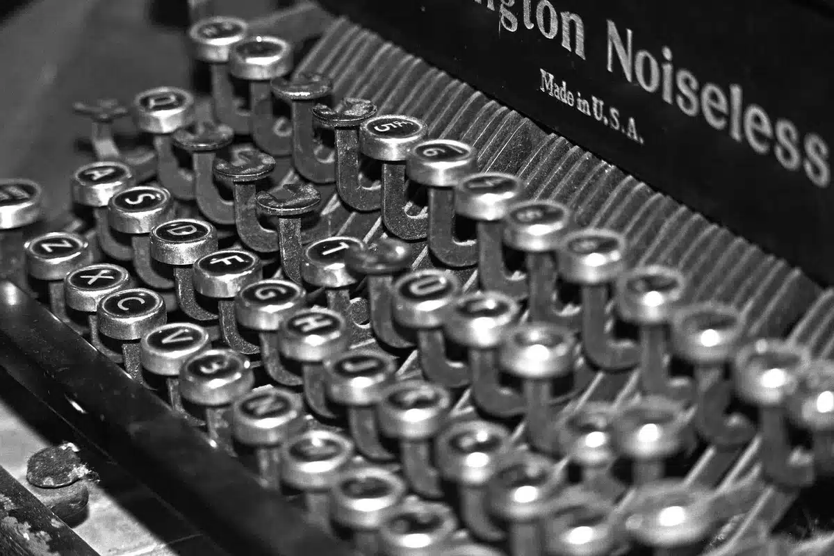 An anonymous creator at a desk surrounded by story notes and paperback books on folklore, hands visible typing on a laptop under a warm lamp — evokes creative development