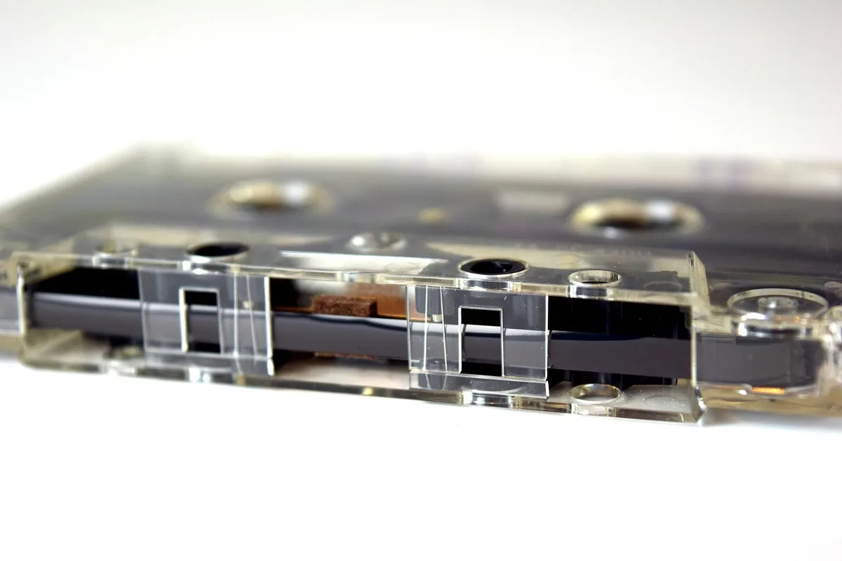 Hands holding a cracked cassette and loose earbuds on a wooden table with music items