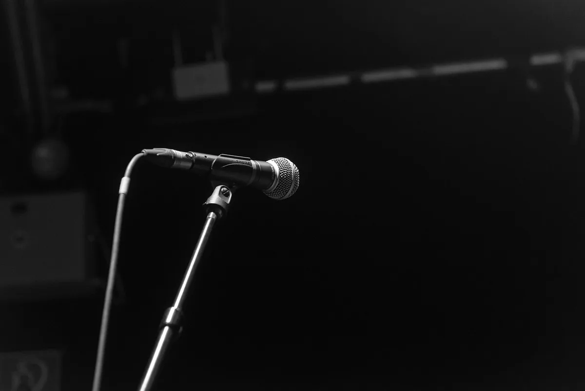 A single empty stage with a lone spotlight and a coiled microphone cable, small pile of clay on the floor suggesting a figure just melted away