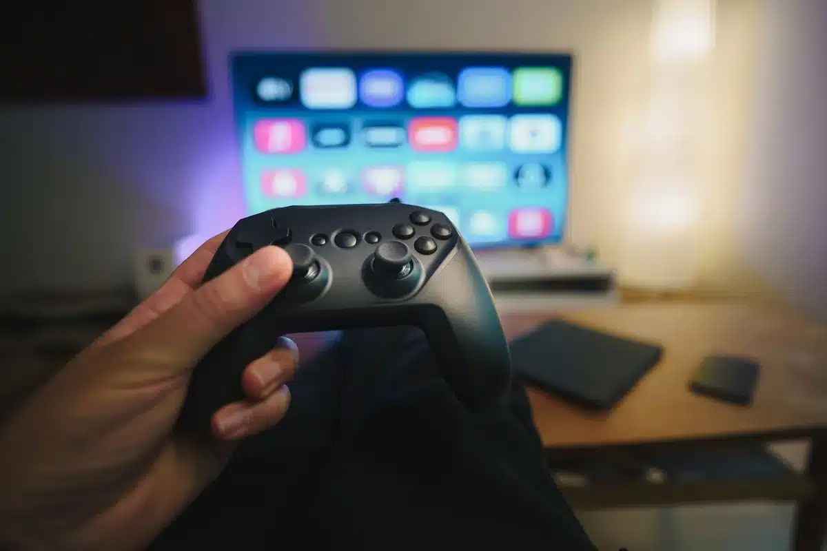 Anonymous hands holding a generic TV remote pointed at a blank flat-screen, couch and lamp blurred in background