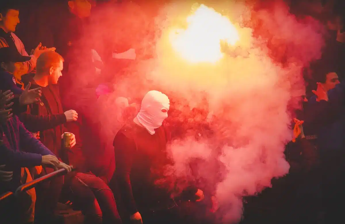 A small crowd of anonymous music fans viewed from behind, dim venue lights and a stage in soft focus, hands raised and a sea of blurred silhouettes