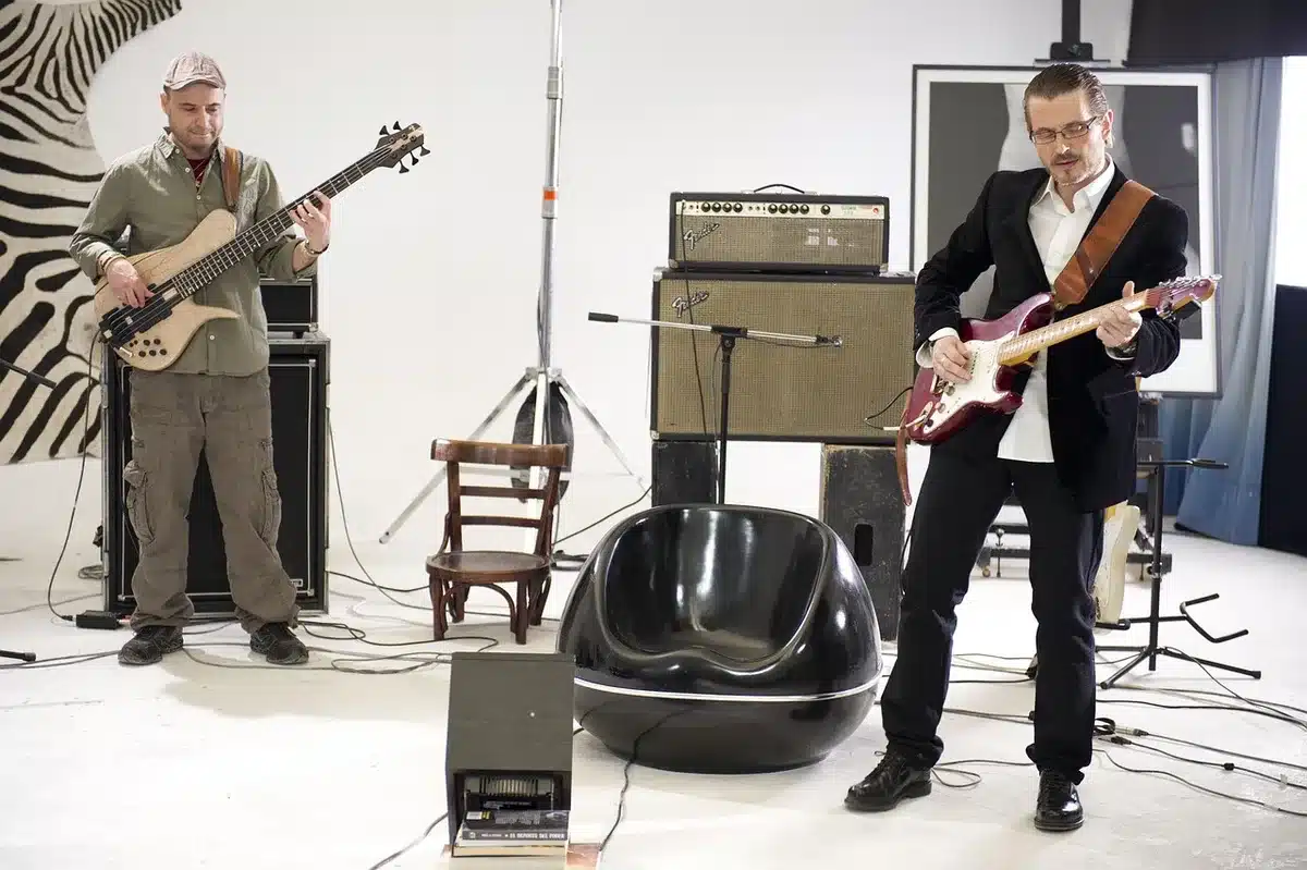 An empty rehearsal studio with a single wooden stool and an unbranded vintage microphone on a stand; stage lights off-camera create soft rim light