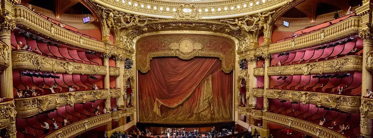 empty proscenium stage with a single spotlight on center, a lone stool and microphone, dark auditorium rows fading into shadow