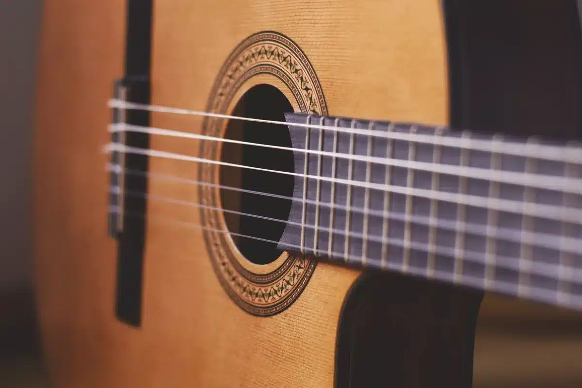A lone acoustic guitar propped against a plain wooden stool on a dim studio floor, an open notebook of handwritten lyrics nearby and a single light overhead — sense of beginning and faith