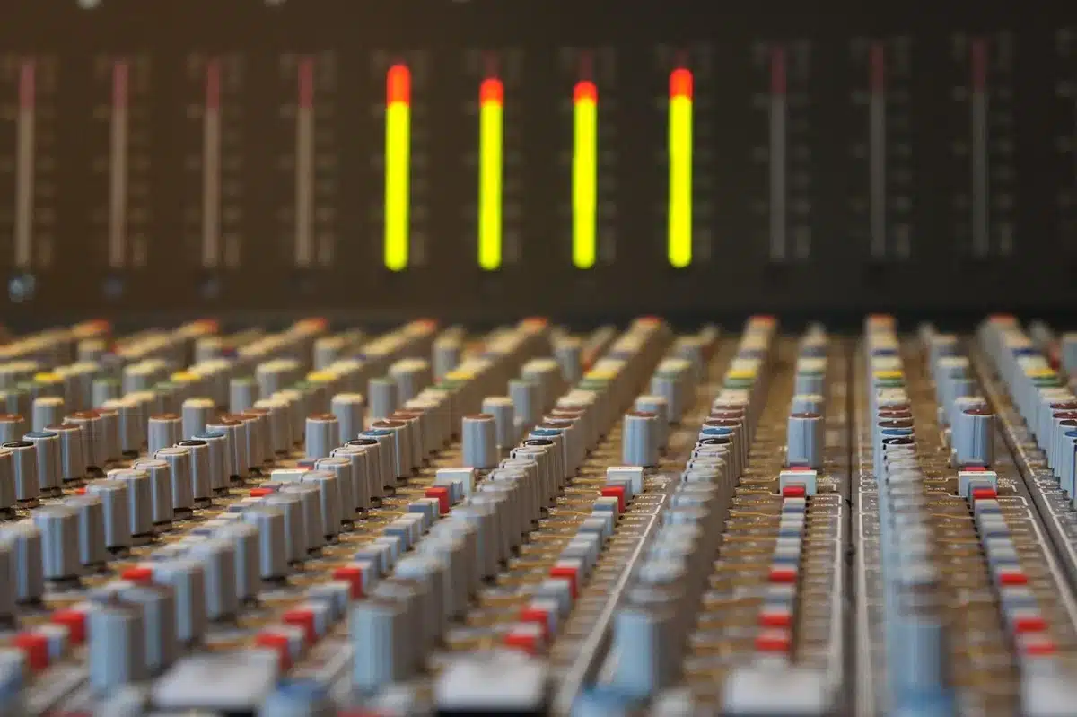 An empty recording-studio control room with a vintage console, a blank vocal booth door ajar and sheet music on a stand — an anonymous music-production setting suggesting a new Christian album.