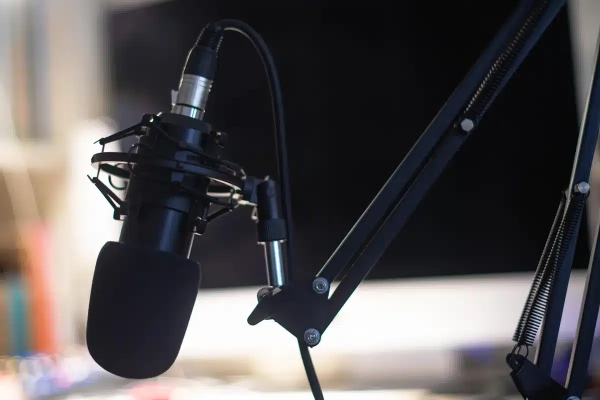 An empty interview studio chair under a single spotlight, a microphone on a stand in the foreground and a pair of anonymous leather boots on the floor nearby