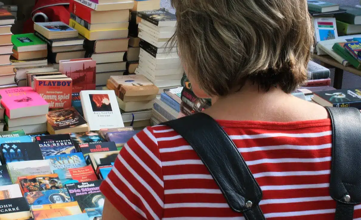 a lone paperback on a café table with a pair of reading glasses and a folded map, sunlight across the cover