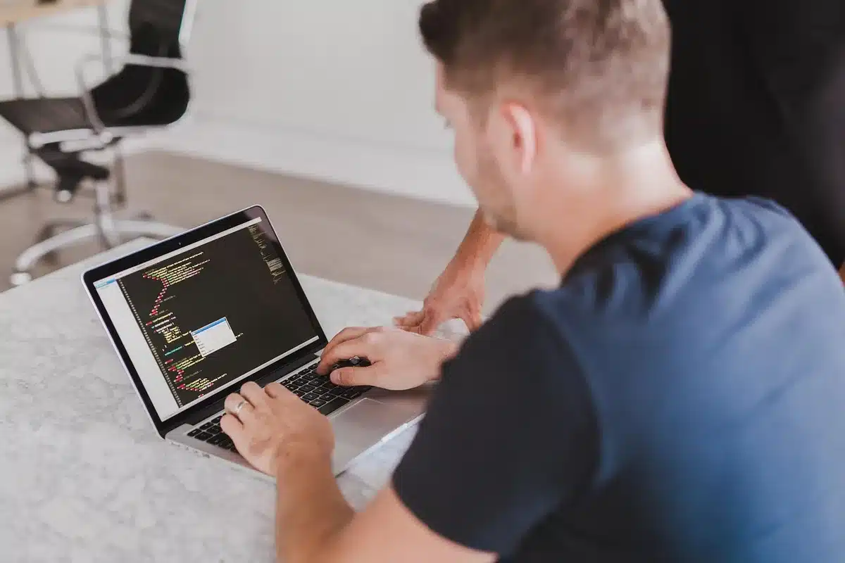 Anonymous person typing at a multi-monitor hacker-style workspace, notes scattered on desk
