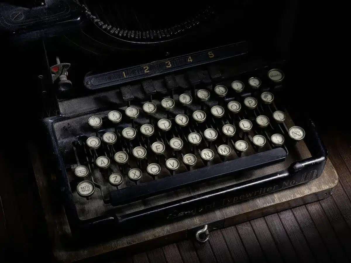 A close-up of an unbranded vintage typewriter atop a pile of cartoon clippings, with an anonymous hand turning a page
