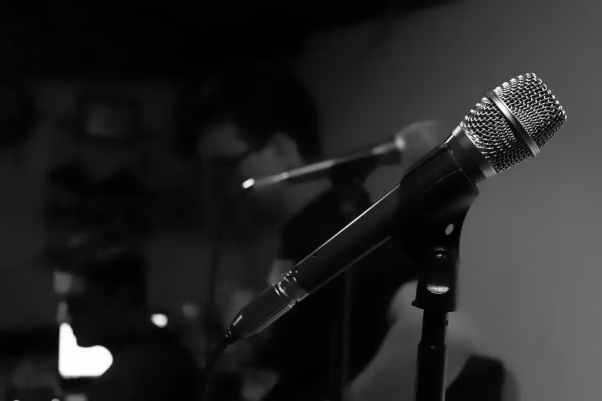 An empty studio microphone on a plain stand under soft spotlight, a coiled cable trailing away into shadow, dust motes visible in the light beam