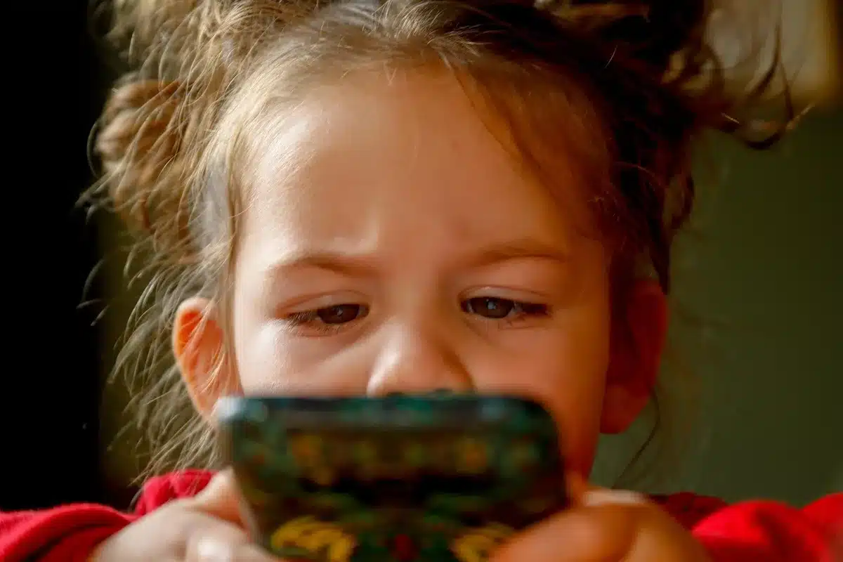 A teenage girl sitting on her bed looking at a ringing phone, tense expression